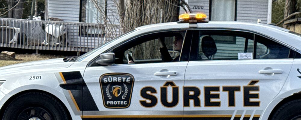 Police SUV with amber roof lights parked in front of a grey house, showing Sûreté logo on the door.
